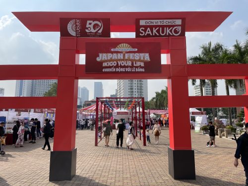 A bright red Japanese shrine gate with Hanoi skyline behind